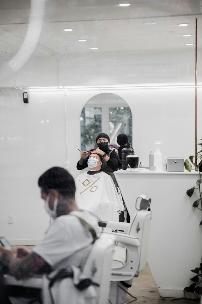 Professional barber in black apron cutting customer's hair in modern barbershop with large mirrors